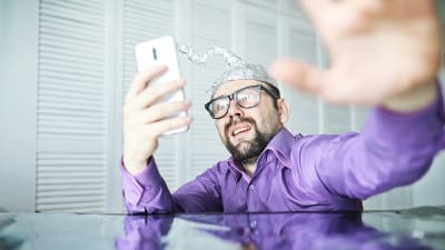 Man med mössa av aluminiumfolie gestikulerar mot sin telefon