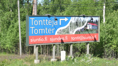 en skylt längs en väg där det står tomter till salu på svenska och finska och sedan sjundeå.fi, siuntio.fi