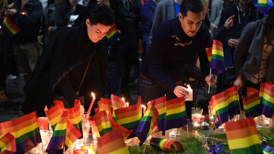 Två personer tänder ljus och placerar regnbågsflaggor bredvid flera regnbågsflaggor vid Taylor Square, i Sydney, Australien. Flera sydneybor samlades för en tyst solidaritetsdemonstration för offren i Orlando.