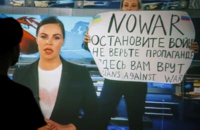 Protest mot kriget i rysk statsstyrd TV, en kvinna bakom nyhetsankaret håller i en skylt med texten "Nej till krig".