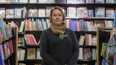En kvinna står mellan hyllorna i en bokhandel och tittar in i kameran.