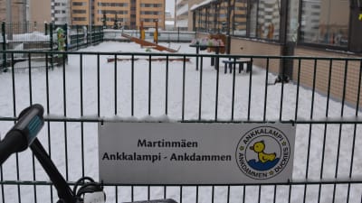 En skylt med texten "Martinmäen Ankkalampi - Ankdammen" på ett staket till ett daghem.