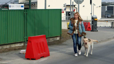 En kvinna i blå jeansdräkt leder en hund i koppel.