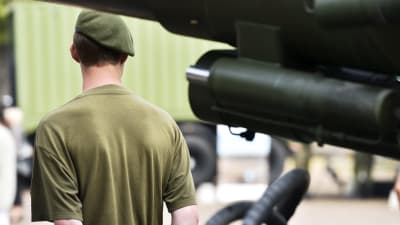 En beväring i grön barett står med ryggen vänd mot kameran händerna knäppta bakom ryggen.