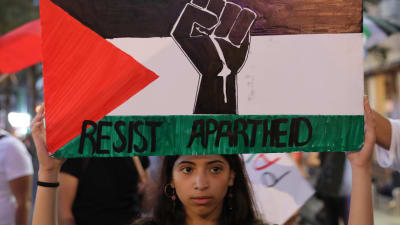 En aktivist håller upp en palestinsk flagga med texten "motstå apartheid" under en protest i Tel Aviv i fjol somras.