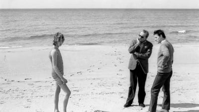 Björn Andrésen poserar på stranden i baddräkt medan regissören och fotografen studerar honom i samband med inspelningen av Döden i Venedig.