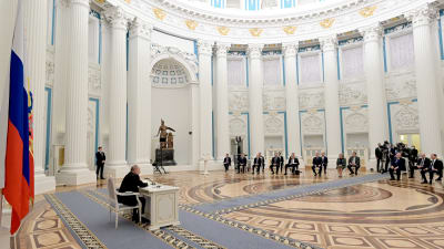 Rysslands president Vladimir Putin sitter i väldig sal. Putins närmaste rådgivare är samlade i en halvcirkel i salens andra ända.