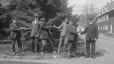 Flera män leker leken "dra fingerkrok" på en väg. Bilden är tagen 1929 i Strömfors bruk.