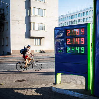 Bild på bensinsstations prisskylt. Bredvid cyklar en man.