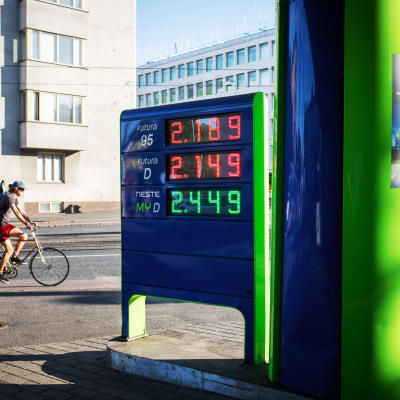 Bild på bensinsstations prisskylt. Bredvid cyklar en man.