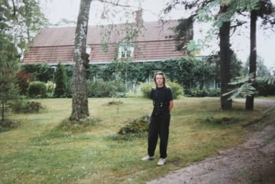 Mustiin vaatteisiin pukeutunut Markus Heikkerö vihreällä nurmella, taustalla puita ja mansardikattoinen huvila.