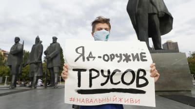 En man i munskydd står bredvid en staty och håller upp en skylt där det på ryska står gift är ett vapen för ynkryggar. Hål dig vid liv Navalnyj. 