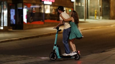 Två personer åker på en elsparkcykel på natten.