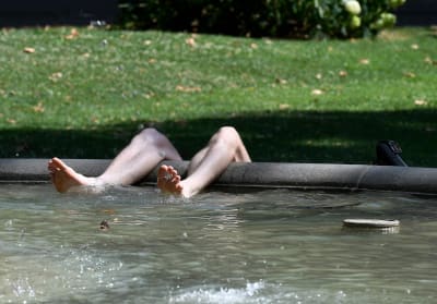 En man som vilar sig i skuggan där bara hans ben och fötter syns som rör i vattnet i en bassäng/fontän.