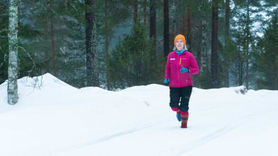 En kvinna springer i skogen genom snön, hon har färggranna yllesockor på fötterna.