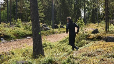 Man i träningskläder springer i skog. I bakgrunden syns spånbana.
