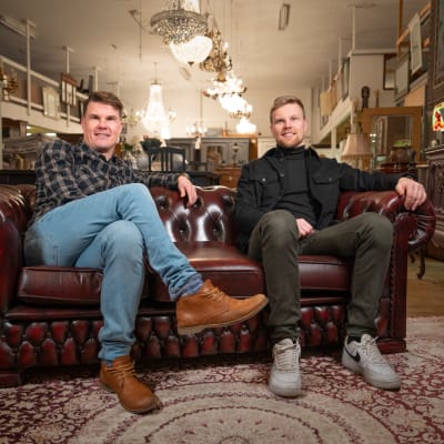 Antiikkikauppiaat Jaakko ja Lauri Kemppainen istuvat liikkeensä keskellä vanhalla antiikkisohvalla.