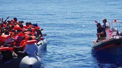 Räddningsarbetare kastar vattenflaskor till flyktingar på en gummibåt på Medelhavet.