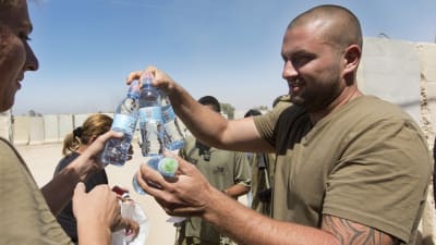 Israelisk soldat delar ut vatten till sina kamrater nära gränsen till Gaza