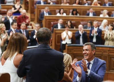 Pedro Sánchez skrattar och klappar i händerna i parlamentet medan andra också står upp och klappar.
