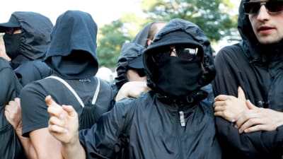 Svartklädda, maskerade demonstranter bildar en "kedja" framför polisen i Hamburg. 