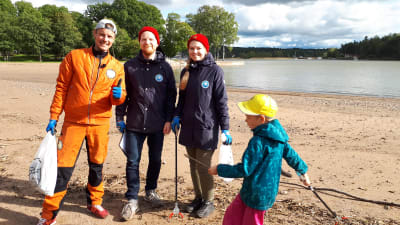 Programledaren Jontti Granbacka står på Runsala strand tillsammans med representanter för Håll Skärgården Ren rfs projekt Snygg beach, på bilden också ett skräpplockande barn