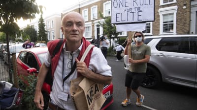Dominic Cummings utanför sitt hem i London i bakgrunden står en demonstrant