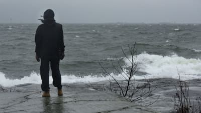 En människa står på ett berg och tittar ut över stormande hav i Helsingfors. 