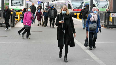 Människor i munskydd på Helsingfors tågstation. I bakgrunden syns tåg.