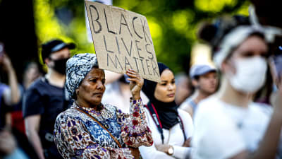 En äldre svart kvinna håller upp en skylt där det står black lives matter.