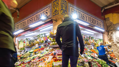 En man står framför en färgglad och ljus frukthandel. Sevilla, södra Spanien.