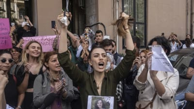På bilden syns kvinnliga demonstranter, kvinnan i mitten håller i en sax och sitt avklippta hår och skriker. 