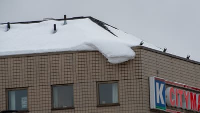 Snö hänger ner från ett höghustak.