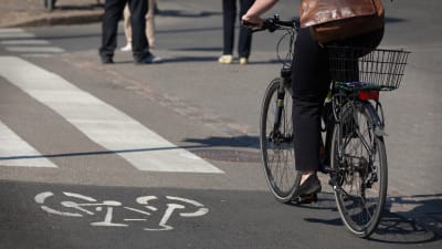 En dam cyklar på sommaren i en stad längs en lättrafikled som korsar en gata.