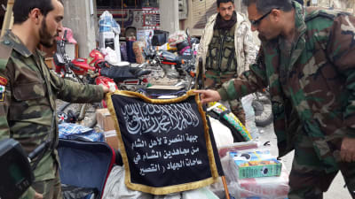 Syriska soldater håller upp en flagg som tillhört jihadistgruppen Jabhat al-Nusra.