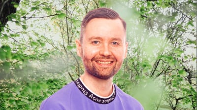 Jakob Höglund småler in i kameran framför en grönskande bakgrund.