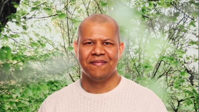 Ari Evwaraye småler in i kameran framför en grönskande bakgrund.