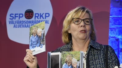 Anna-Maja Henriksson viftar med ett valprogram framför en SFP-logo.