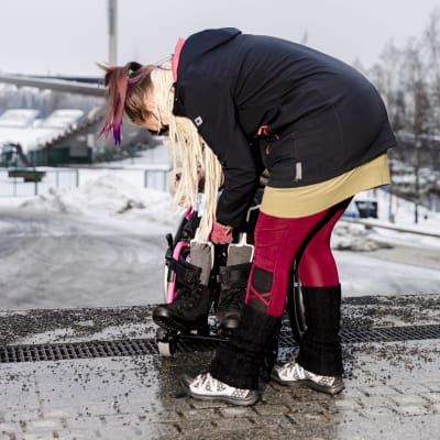 Avustaja avustaa naista pyörätuolissa ulkona, taustalla näkyy Tampereen Ratinan stadion. 