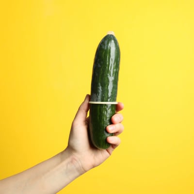 En hand håller i en gurka med en kondom.