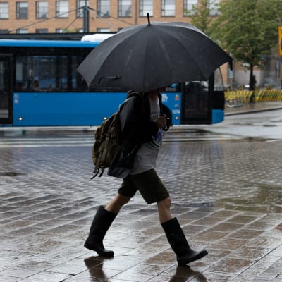Ihminen kävelee sateella kaupungissa, pää hautautuneena sateenvarjoon. 