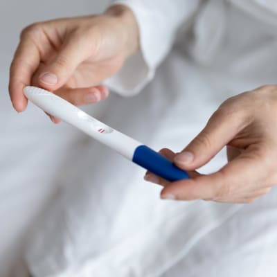 Två händer som håller i ett graviditetstest som visar två streck - alltså en graviditet.