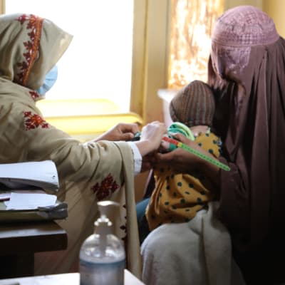Sairaanhoitaja tarkastaa pienen lapsen kuntoa terveysasemalla Afganistanissa.
