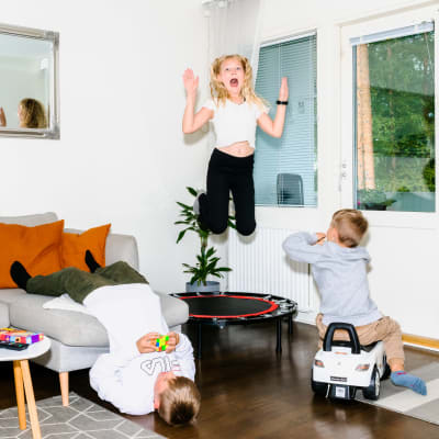 Tuukka pyörittelee Rubikin kuutiota sohvalla pää alaspäin, Mia hyppii trampoliinilla ja huutaa, Jare ajaa pienellä leikkiautolla olohuoneessa.