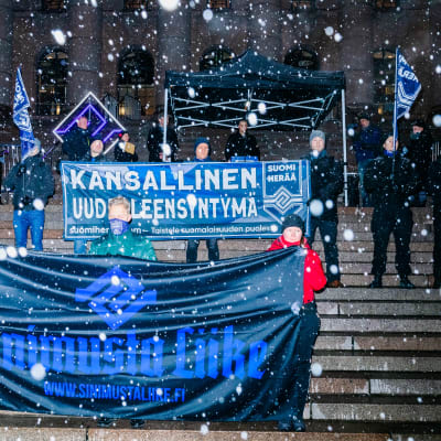 Äärioikeiston mielenosoittajia Suomen lippujen ja iskulauseiden kanssa eduskuntatalolla.