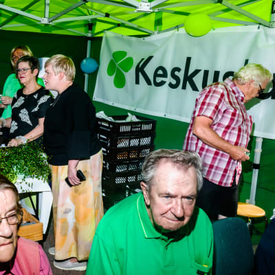 Annika Saarikko står i ett Centern-tält på ett torg och diskuterar med väljare.