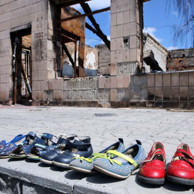 Rivi lasten kenkiä. Taustalla tuhoutunut rakennus.