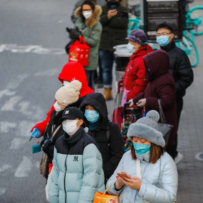 Folk med munskydd  som väntar på en buss i Peking i december 2022