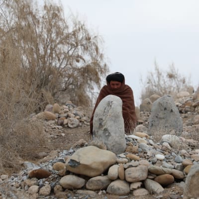  Shaaliin kääriytynyt mies istuu suuren kiven edessä hautausmaalla.