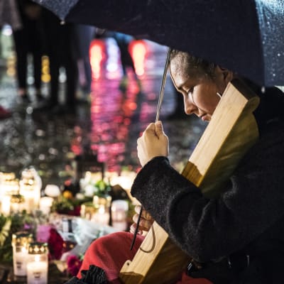 Ung kvinna med mörkt hår spelar på kanteleliknande instrument vid gravljusen och blommorna på Åbo salutorg efter knivdådet den 18.8.2017